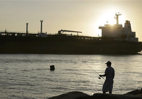 An oil tanker passes a fisherman as it enters a channel near Port Aransas, Texas, early Tuesday, July 21, 2015