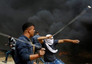Palestinian protestors uses slings to throw stones towards Israeli forces during clashes across the border, following a demonstration calling for the right to return