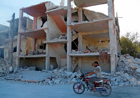 A Syrian man rides a motorcycle past a destroyed building in the district of Jisr al-Shughur, in the Idlib province