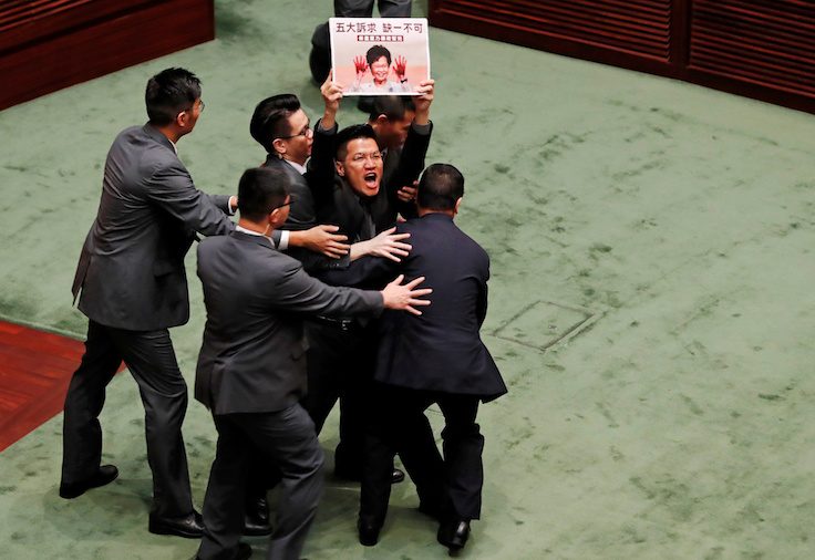 A pro-democracy lawmaker holding a placard is escorted by security from the Legislative Council
