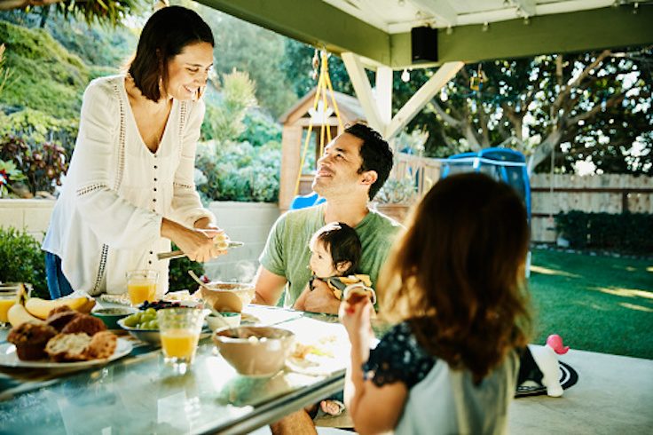Smiling mother and father sharing breakfast with young family at table in backyard